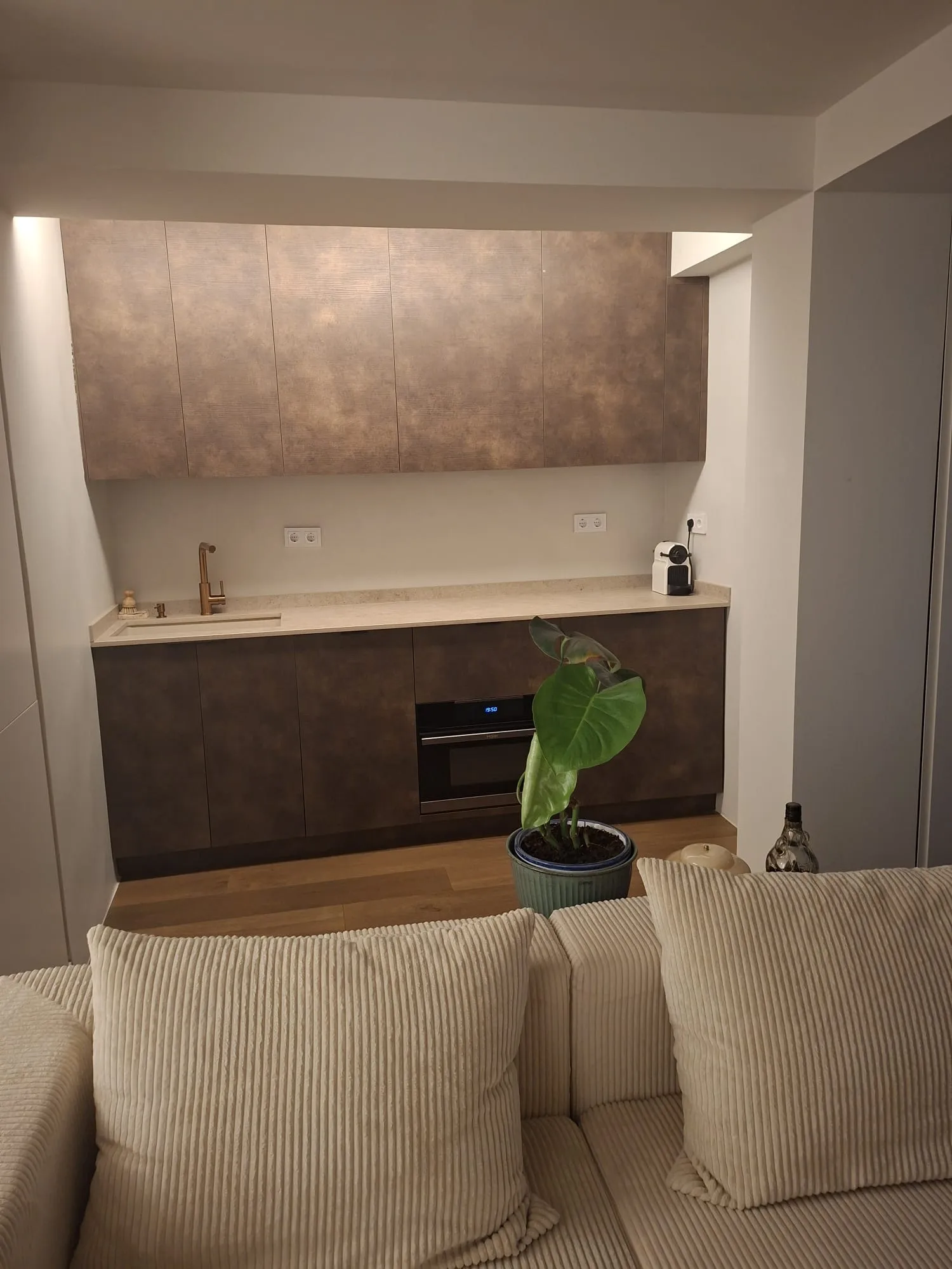 Cocina terminada por Brandum con muebles en acabado cobre, encimera clara y suelo de madera